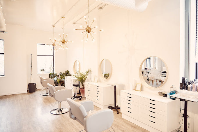 Salon chair and stations with round mirrors line a bright white wall in Luxe Beauty Company. 