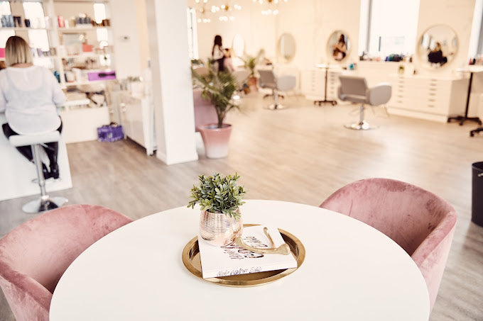 Salon view with table and pink velvet chairs in the forefront of the picture at Luxe Beauty Company. 